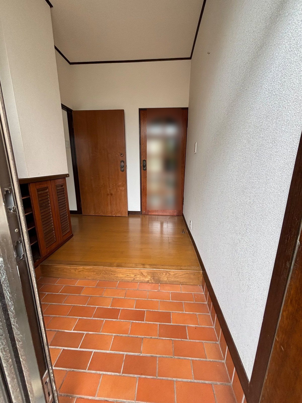 作業後の1階の住戸の玄関。オレンジ色のタイルの土間と板の間に物は残っておらず、奥に木の扉が2つある